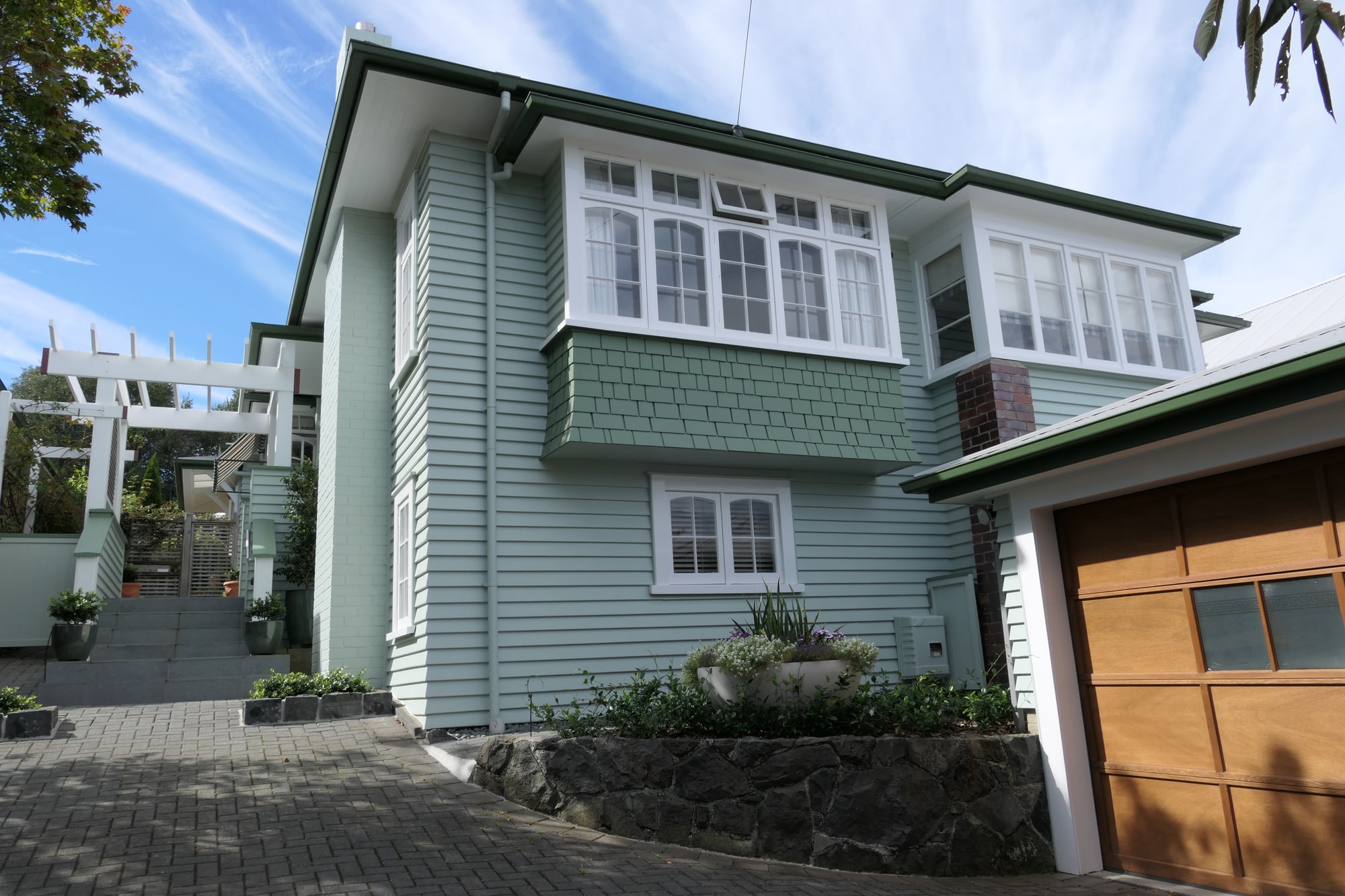 A pale green weatherboard villa with white joinery, photographed against a blue sky.