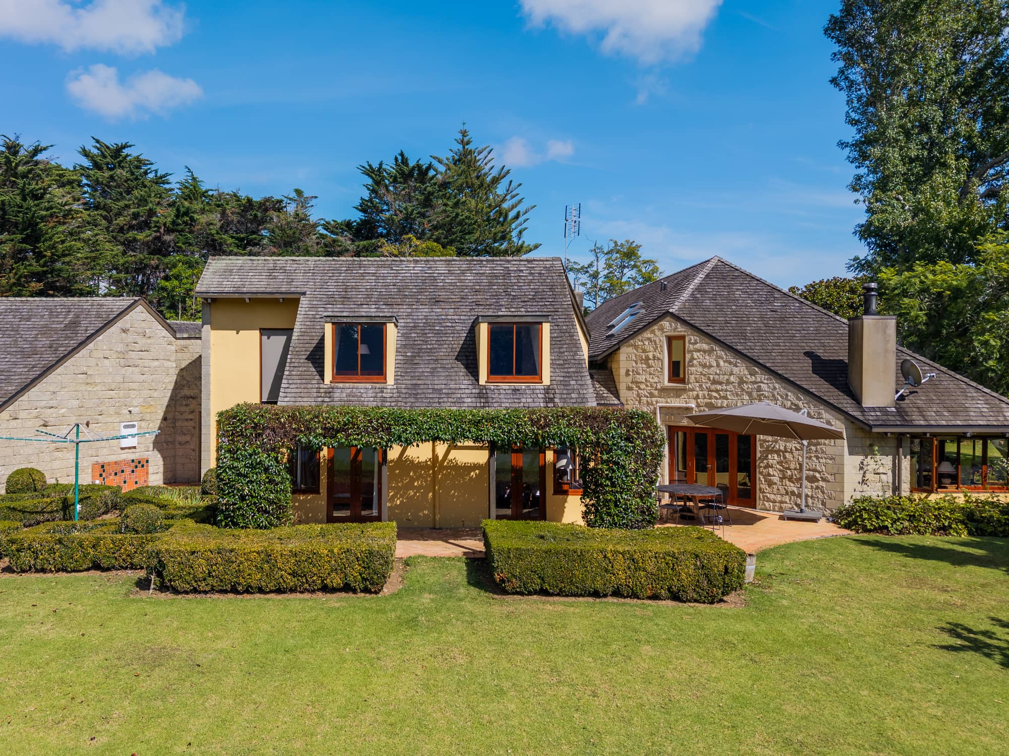 A stone and render country house with varnished timber joinery throughout, seen across a clipped garden.